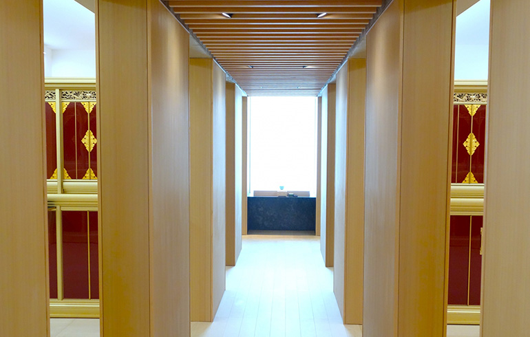 Wood-paneled hallway with tall vertical columns leading to a bright window at the far end of the corridor