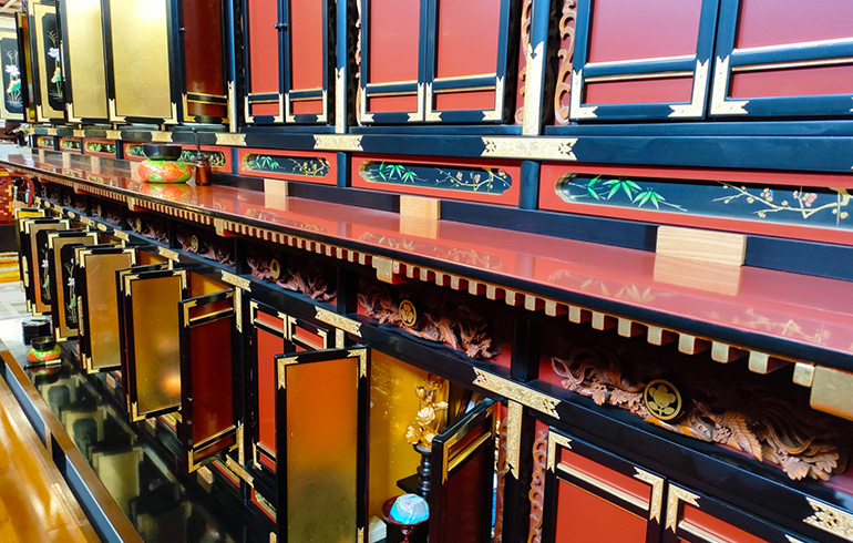 Row of ornately lacquered red, gold, and blue drawers and cabinets arranged along a shelf, like a traditional altar display